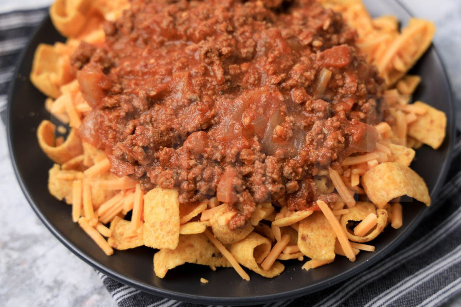 The Frito Pie comes on a gray plate with a gray striped napkin on a marble backdrop.