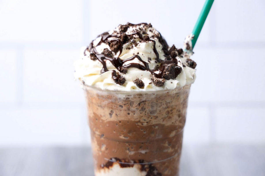 The Mocha Cookie Crumble Frappuccino comes in a venti cup with a white striped napkin on a gray wood backdrop.