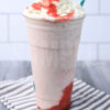 The Strawberry Crème Frappuccino comes in a venti cup with a white striped napkin on a gray wood backdrop.