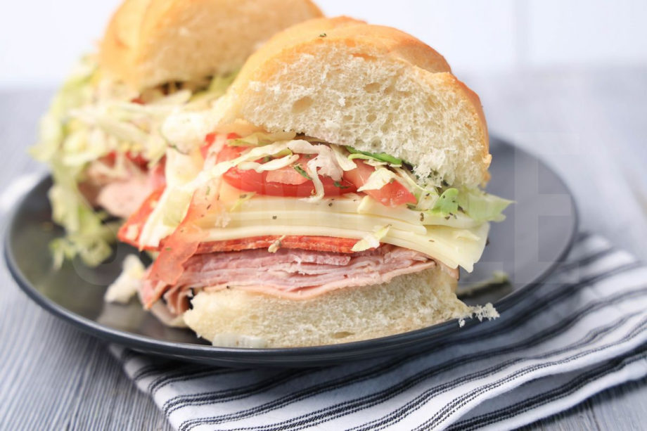 The Italian Grinder sandwich comes on a gray plaid with white striped napkin on a gray wood backdrop.