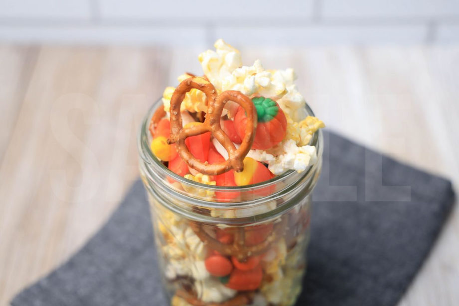 The Fall Snack Mix comes in a mason jar with a denim napkin on a  rustic wood backdrop.