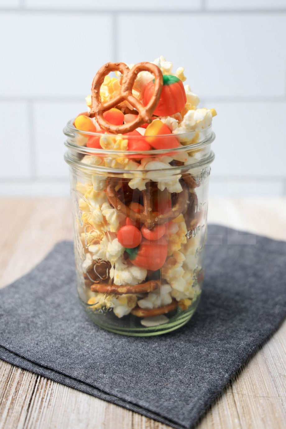 The Fall Snack Mix comes in a mason jar with a denim napkin on a  rustic wood backdrop.