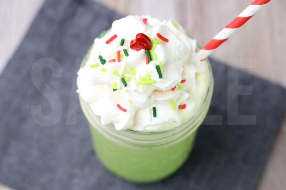 Grinch Hot Chocolate comes in a glass with a denim napkin on a rustic wood backdrop.