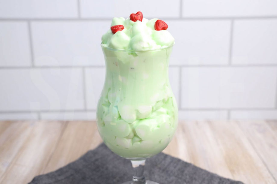 The Grinch Fluff comes in a clear glass with a denim napkin on a rustic wood backdrop.