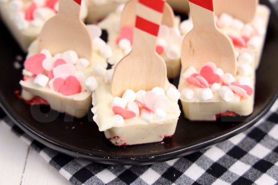 The Strawberry White Hot Chocolate Spoons comes on a black plate with a plaid napkin on a white wood backdrop.