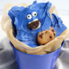 The Cookie Monster Bark comes in a blue pail with parchment paper with a blue and white striped cloth on a white wood backdrop.