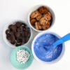 The Cookie Monster Bark comes in a blue pail with parchment paper with a blue and white striped cloth on a white wood backdrop.