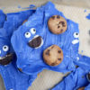 The Cookie Monster Bark comes in a blue pail with parchment paper with a blue and white striped cloth on a white wood backdrop.