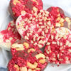 The Heart Raspberry Nut Chocolates comes on a white plate with a white and red heart cloth on a gray wood backdrop.