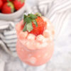 The Strawberry Fluff comes in a clear glass with a white and dark gray cloth on a marble wood backdrop.