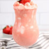 The Strawberry Fluff comes in a clear glass with a white and dark gray cloth on a marble wood backdrop.