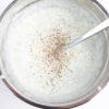 The Tzatziki Dip comes in a white bowl on a wood cutting board with a olive green cloth on a white wood backdrop.