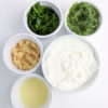 The Tzatziki Dip comes in a white bowl on a wood cutting board with a olive green cloth on a white wood backdrop.