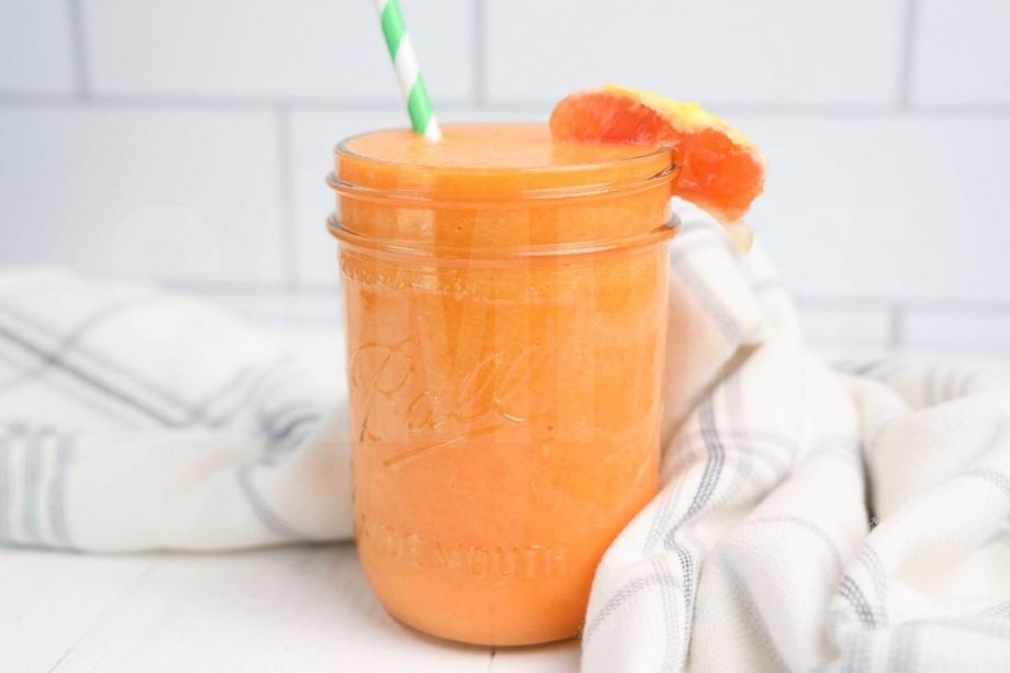 The Carrot Apple Orange Smoothie comes in a mason jar with a grey and white plaid cloth on white wood backdrop.