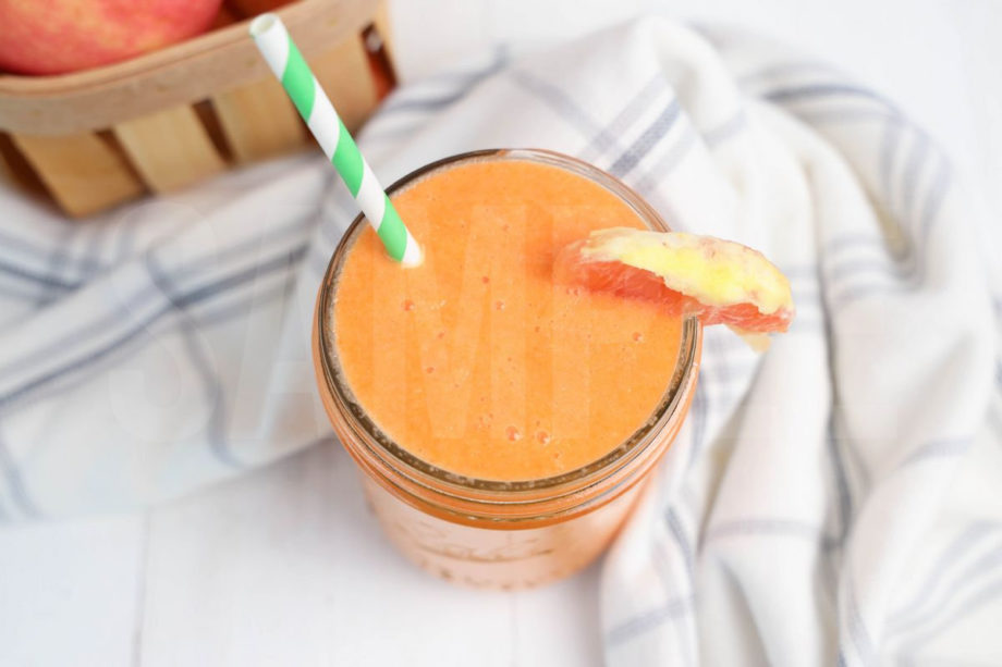 The Carrot Apple Orange Smoothie comes in a mason jar with a grey and white plaid cloth on white wood backdrop.