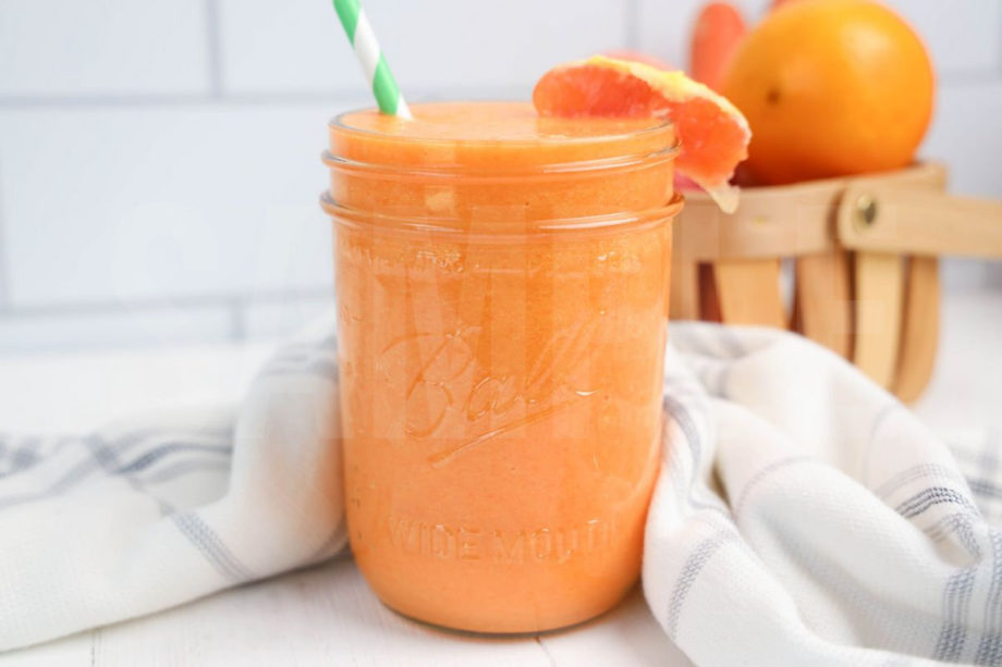 The Carrot Apple Orange Smoothie comes in a mason jar with a grey and white plaid cloth on white wood backdrop.