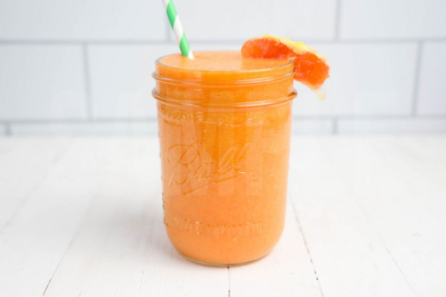 The Carrot Apple Orange Smoothie comes in a mason jar with a grey and white plaid cloth on white wood backdrop.