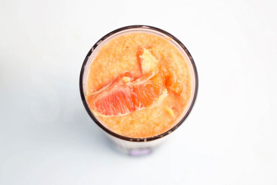 The Carrot Apple Orange Smoothie comes in a mason jar with a grey and white plaid cloth on white wood backdrop.