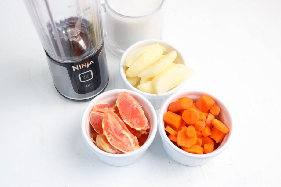 The Carrot Apple Orange Smoothie comes in a mason jar with a grey and white plaid cloth on white wood backdrop.