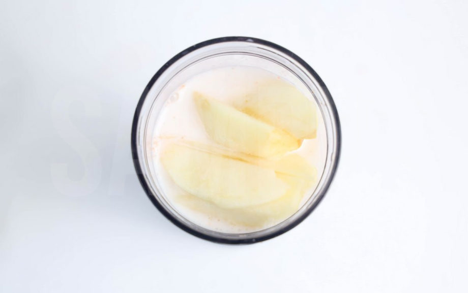 The Carrot Apple Orange Smoothie comes in a mason jar with a grey and white plaid cloth on white wood backdrop.