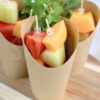 The Melon Fruit Cups comes in a brown fry cup with rustic wood backdrop.