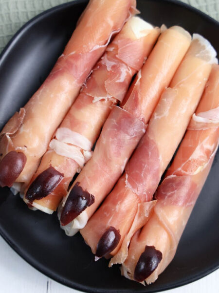 The Prosciutto Witch Fingers come on a gray plate with white wood backdrop.